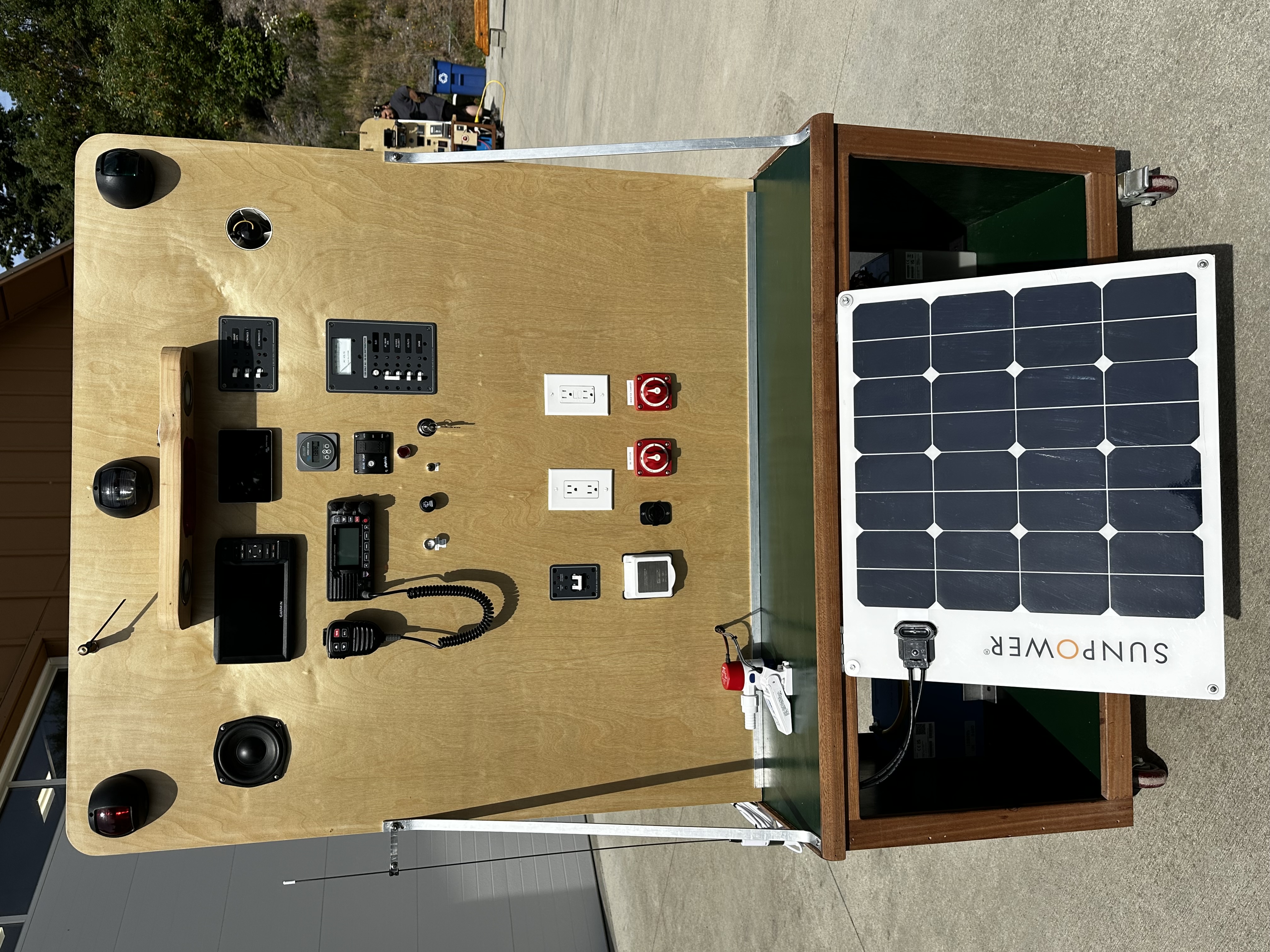 Board 2 helm side showing Garmin MFD, VHF radio with external speaker, navigation lighting, battery switches, distribution panel, and SunPower solar panel